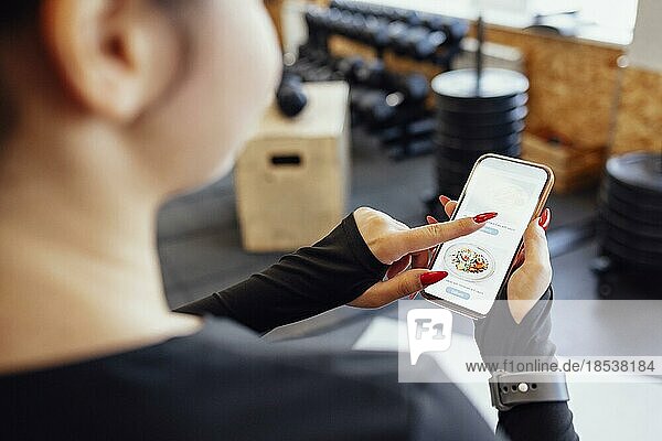 Fitness App. Sporty Fit Young Lady Holding And Pointing At Smartphone With fitness app While Training indoors. Smiling Woman Demonstrating screen of mobile phone