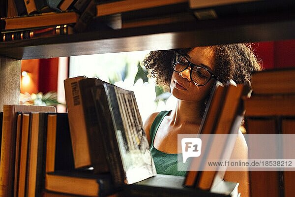 Glückliche afroamerikanische Studentin  die in der Universitätsbibliothek studiert und nach einem Buch sucht  mit Brille