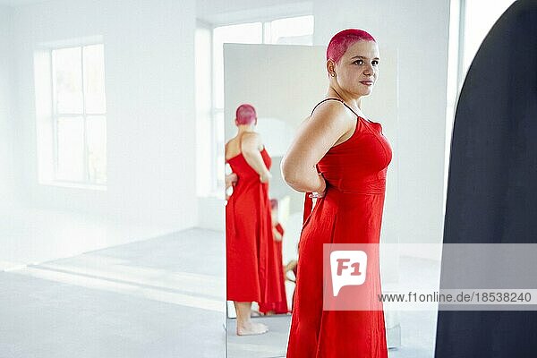 Schöne entspannte Frau in rotem langen Kleid und roten Haaren schaut in den Spiegel. Konzept der Körper positiv