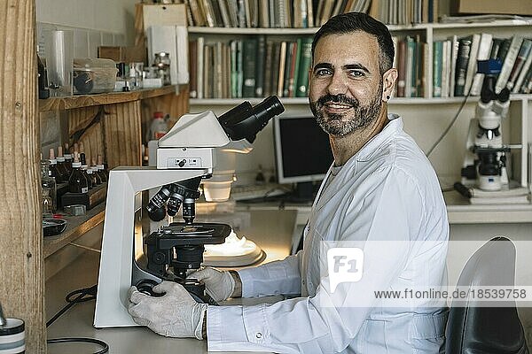 Scientist in front of microscope  smiling and looking at camera