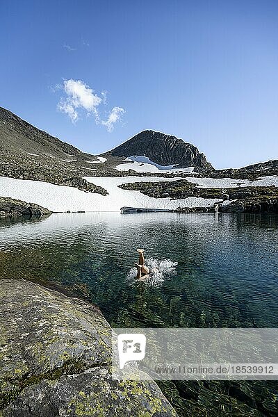 Young man jumps into a mountain lake  Skålavatnet  ascent to the summit of Skåla  Norway  Europe