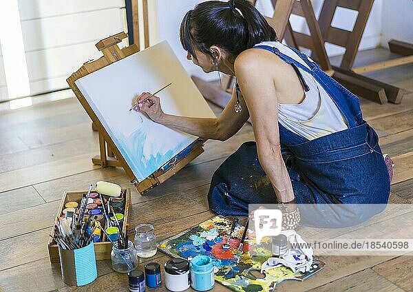Frau Künstlerin malt auf einer Leinwand ein blaues abstraktes Bild. Kreative Frau arbeitet auf dem Boden in ihrem Kunstatelier