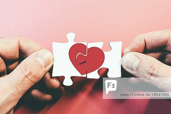 Hände  die Puzzleteile mit rotem Herz  Liebe oder gebrochenem Herz verbinden oder trennen