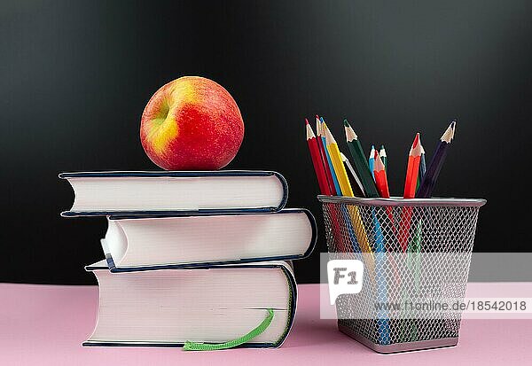 Bildungskonzept  frischer Apfel auf Stapel von Büchern neben Bleistiftbecher mit Buntstiften