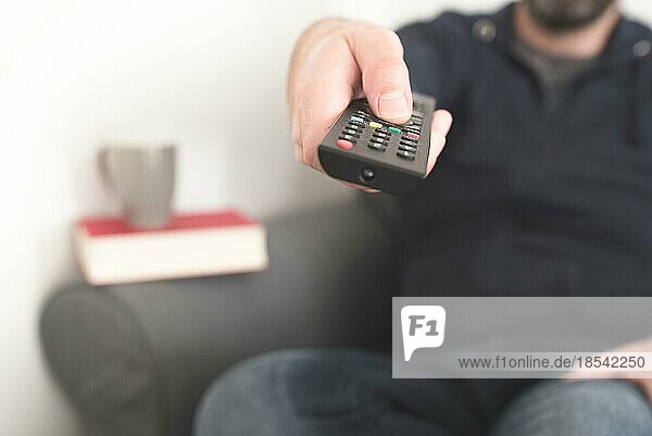 Vorderansicht einer auf dem Sofa sitzenden Person  die mit der Fernbedienung des Fernsehers den Sender wechselt