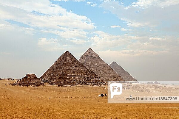 Blick auf das Gizeh-Plateau mit Touristen und Einheimischen  die auf Kamelen reiten  und die Große Pyramide im Hintergrund an einem dunstigen Tag  Kairo  Ägypten  Afrika