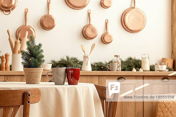 Zwei Teetassen auf einem Weihnachtstisch mit einem kleinen Baum in einer hellen  modern dekorierten Küche mit vielen Kupferpfannen an der Wand  Küchengeräten und -utensilien  Kerzen  Platz für Text