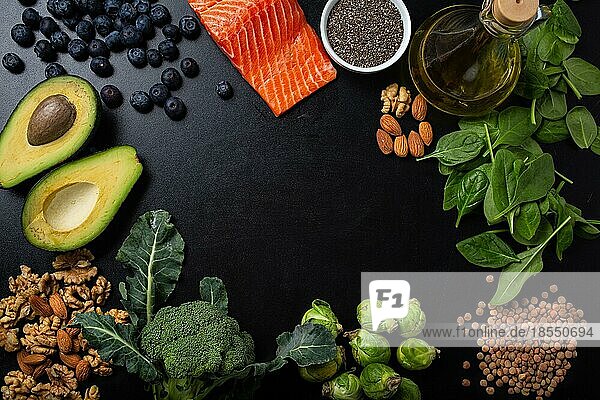 Gesundes Essen Hintergrund mit guten Fettquellen  Zutaten reich an Omega-Fettsäuren: Lachsfilet  Gemüse  Beeren  Nüsse  Samen  Olivenöl  schwarze Kreidetafel Draufsicht  Platz für Text