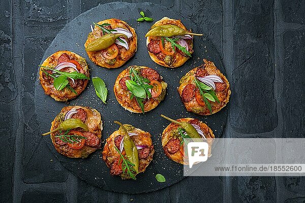Hausgemachte kleine Pizza mit Pesto  Salami  Tomaten und Rucola auf schwarzem Hintergrund