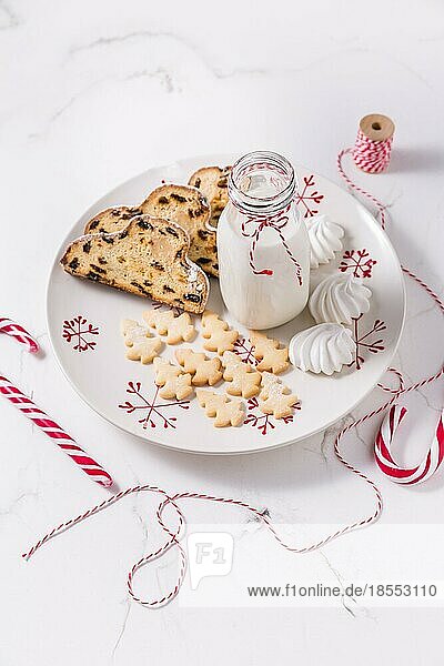 Flasche Milch mit traditionellem Christstollen  kleinen Keksen und Zuckerstangen auf weißem Hintergrund. Deutsches Weihnachtsbrot
