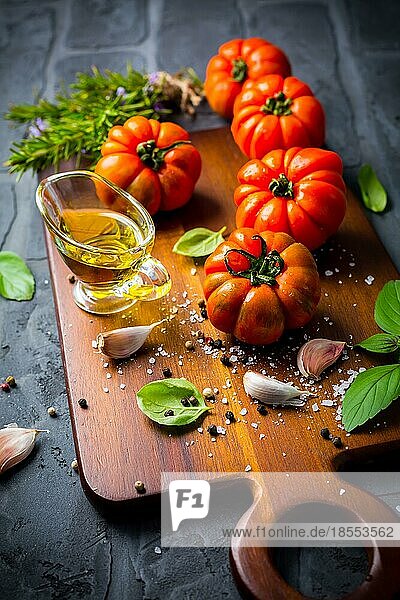 Italienische Küche Olivenöl  Tomaten und Kräuter auf einem rustikalen Schneidebrett