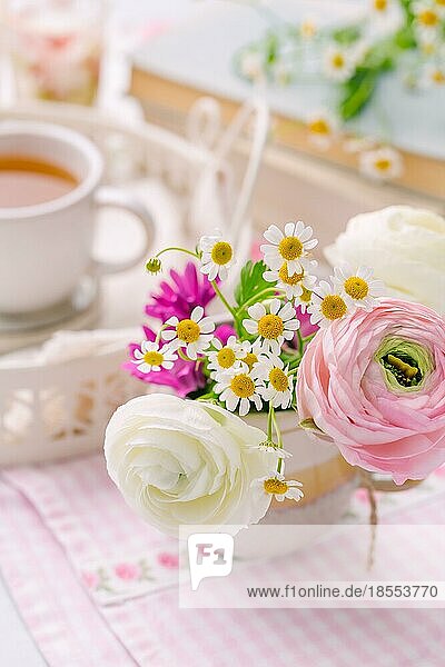 Schöne zarte Blüte von frischen Schnitt Blumenstrauß mit Tasse Tee nad Bücher im Hintergrund auf dem Küchentisch