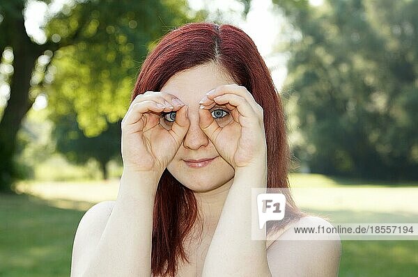 Junge Frau imitiert ein Fernglas mit ihren Fingern um die Augen