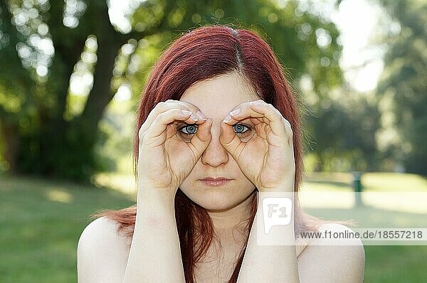 Junge Frau imitiert ein Fernglas mit ihren Fingern um die Augen