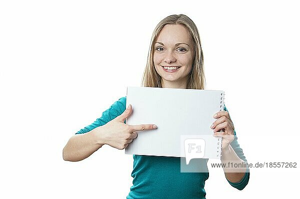 Glückliche junge blonde Frau  die ein leeres Schild hält und auf eine Werbefläche zeigt