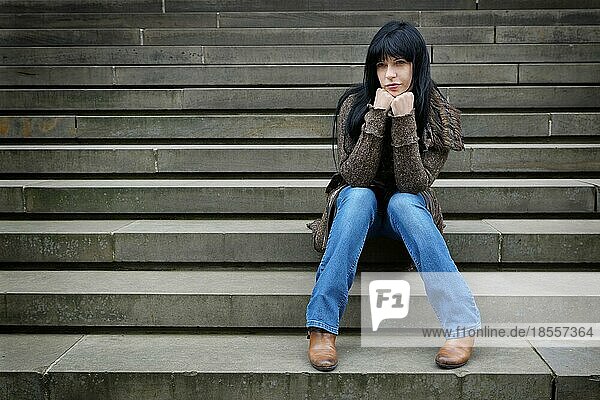 Einsame Frau  die draußen auf den Stufen sitzt