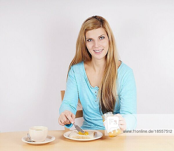 Junge Frau  die sich am Frühstückstisch Marmelade auf ihren Toast schmiert