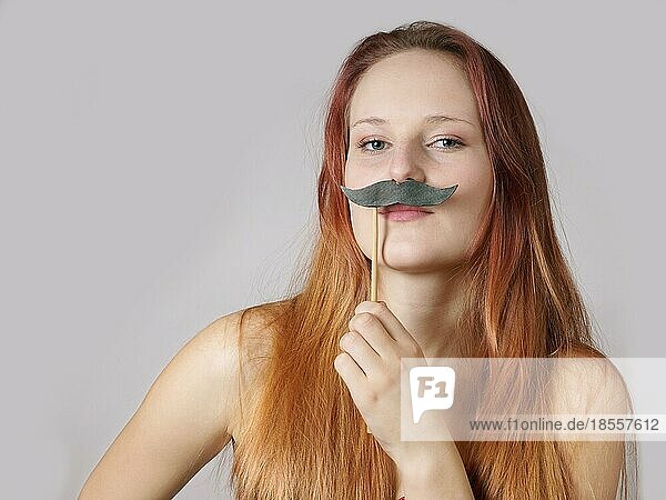 Junge Frau hält sich einen falschen Schnurrbart an einem Stock ins Gesicht