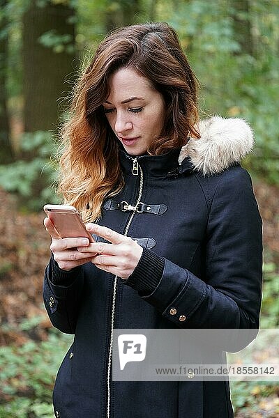 Junge Frau  die ein Handy oder Smartphone benutzt  während sie draußen im Wald ist