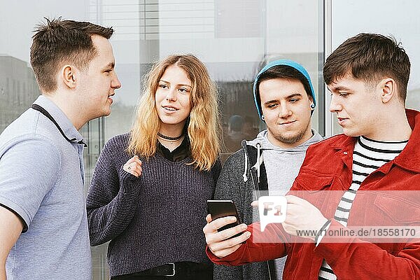 group of teenage friends having a conversation or discussion  young man is showing something on his smartphone