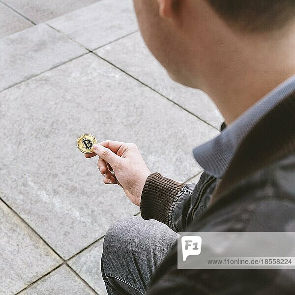 Unkenntlicher junger Mann hält Bitcoin-Münze in der Hand  Kryptowährung Hype-Konzept