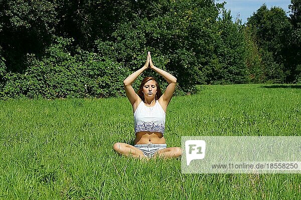 Junge Frau übt Yoga-Meditation im Freien auf einer Wiese