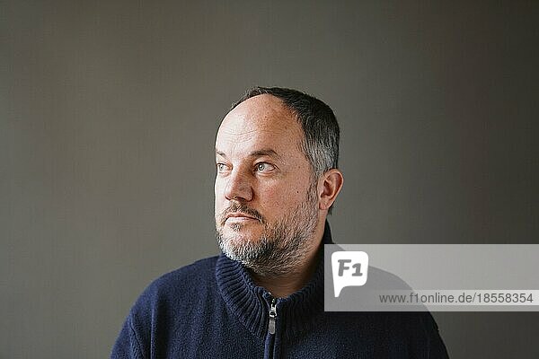 50 year old man with graying hair and beard looking away thinking - grey wall background with copy space