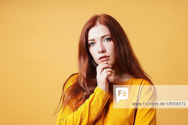 Nachdenklich junge Frau mit Finger auf Kinn Geste - gelb orange Farbe Hintergrund mit Kopie Raum