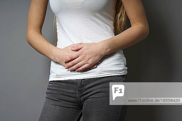 unrecognizable young woman holding her stomach with both hands - concept for dysmenorrhea  abdominal pain  irritable bowel syndrome  belly or stomach ache  painful periods or menstrual cramps