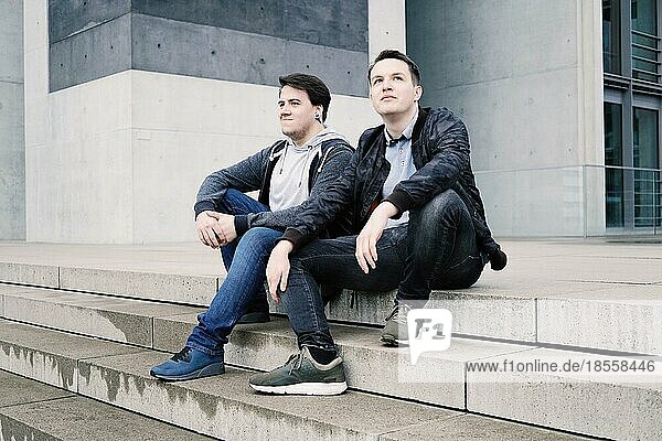 two male teenage friends or brothers two male teenage friends sitting on concrete steps or staircase outside - urban youth lifestyle