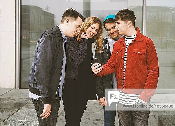 young man showing something on his mobile phone to a group of friends - urban teenage lifestyle