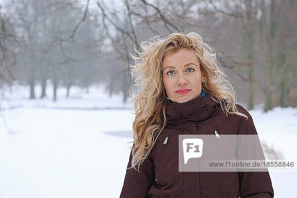blond woman standing in snow covered park in winter