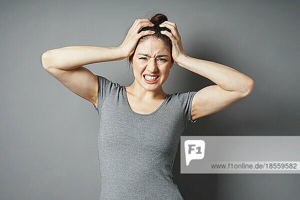 Gestresste junge Frau in Verzweiflung oder Schmerz mit Händen  die den Kopf halten - grauer Hintergrund mit Kopierraum