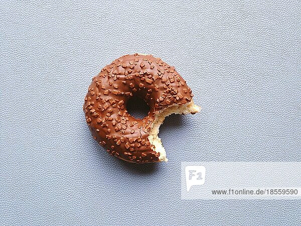 Schokoladenglasierter Donut oder Krapfen mit fehlendem Biss - Draufsicht auf blauem Hintergrund mit Kopierraum