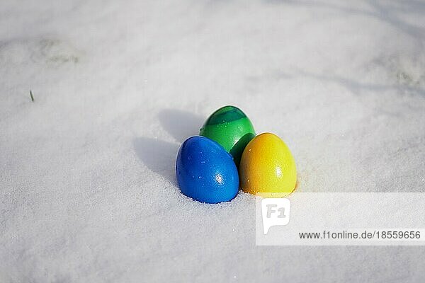 Drei in leuchtenden Farben bemalte Ostereier liegen im frischen Schnee
