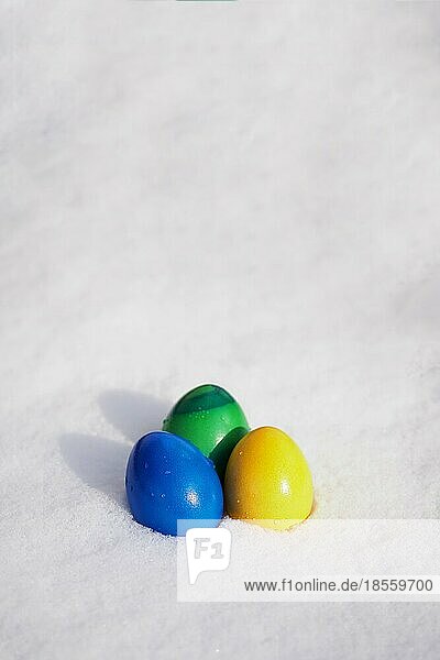 Drei in leuchtenden Farben bemalte Ostereier  die im frischen Schnee liegen  vertikaler Hintergrund mit Kopierraum