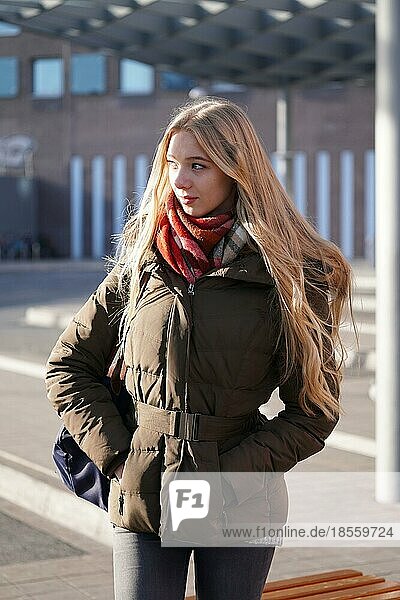 candid street style image of young woman waiting at bus station on a sunny day in winter