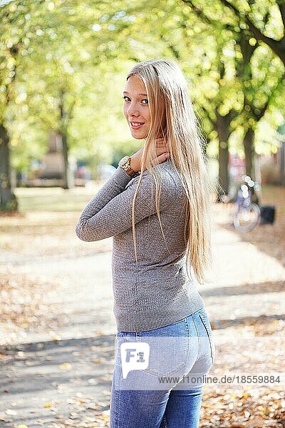 Teenager-Mädchen genießt den sonnigen Tag im Park - Rückansicht einer jungen Frau in Jeans und Pullover  die den Kopf herumdreht