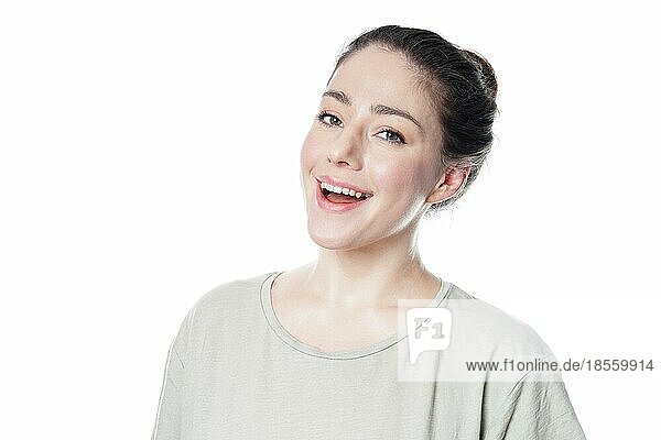 Fröhliche junge Frau in den 20ern mit natürlichem Make-up und brünettem Haarknoten  lächelnd - vor weißem Hintergrund