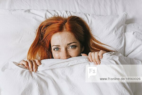 Schüchterne junge Frau  die sich unter der Bettdecke versteckt und schüchtern wirkt