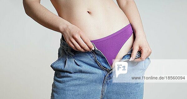 Mittelteil einer nicht erkennbaren Frau in offenen Jeans  die sich auszieht und ein lila Höschen zeigt  als Konzept für die Gesundheit von Frauen oder die weibliche Sexualität