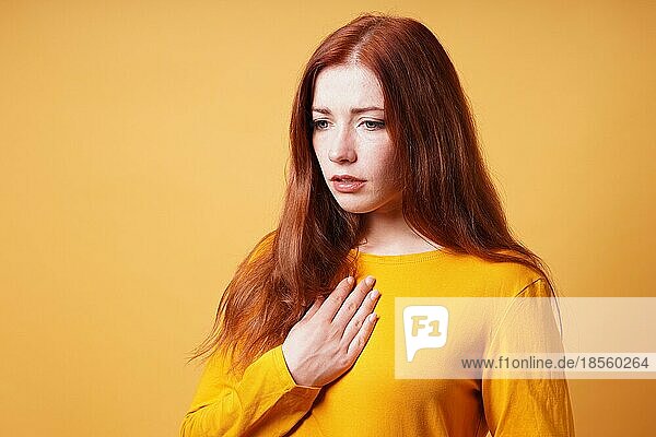 Traurige junge Frau mit der Hand auf der Brust  die sich wegen Herzschmerz oder Sodbrennen krank fühlt