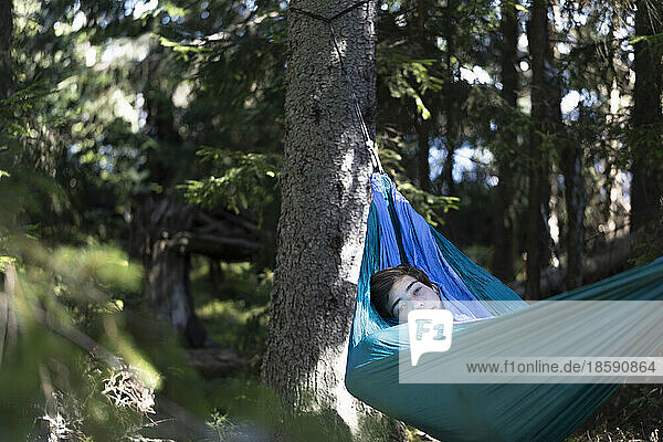 Boy (16-17) relaxing in hammock in forest