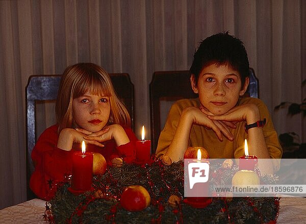 2 zwei Kinder sitzen am Adventskranz  4 vier brennende Kerzen  Weihnachtszeit  Advent  2 two children sit in the Advent wreath  4 four burning candles  yule tide