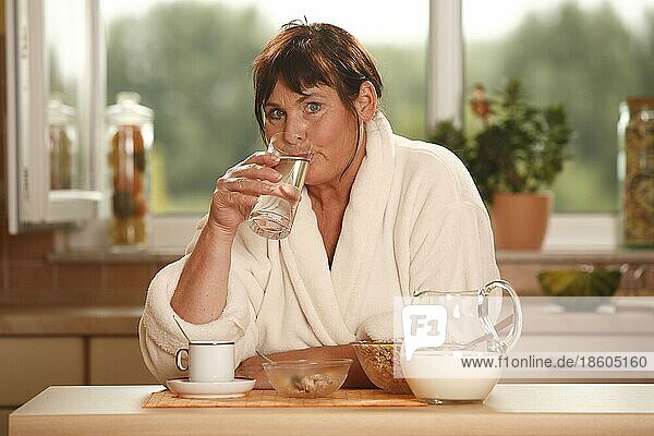 Frau beim Frühstück trinkt Glas Wasser  Frühstück  frühstücken  Kanne Milch  Schüsseln  Müsli  Tasse Kaffee  frühstückt