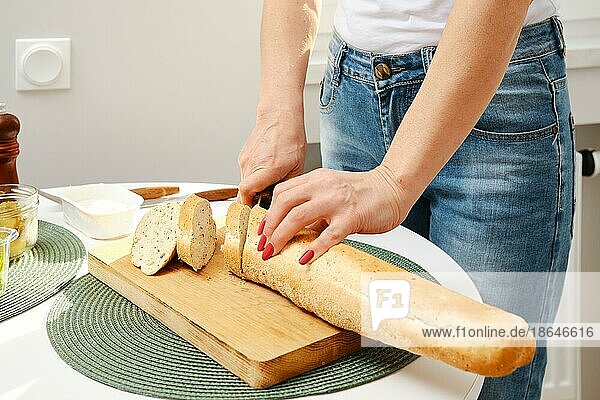 Nahaufnahme von Frauenhänden  die frisches Baguette in Scheiben schneiden