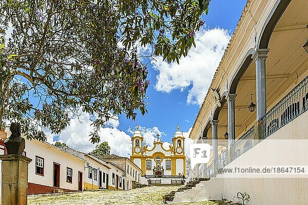 A quiet historic cobblestone street in the city of Tiradentes in Minas Gerais with colonial houses and a baroque church in the background  Brasil