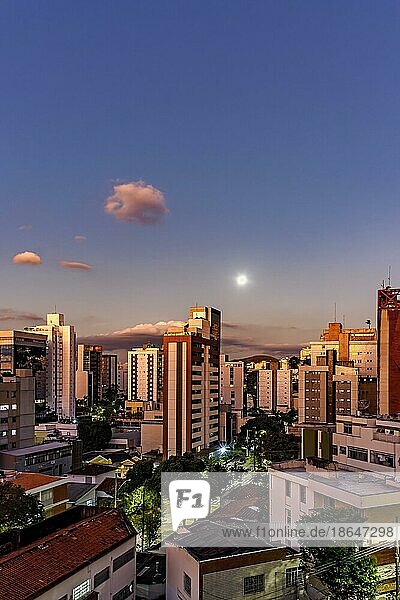 District of the city of Belo Horizonte in Minas Gerais with its buildings lit up by the sunset and with the full moon rising in the background  Brasil