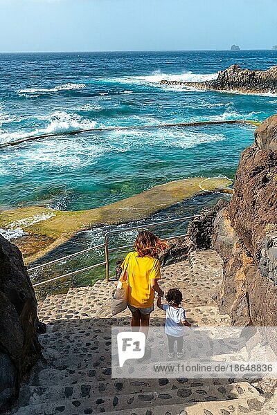 A mother with her son going down into the La Maceta rock pool on the island of El Hierro in the Canary Islands