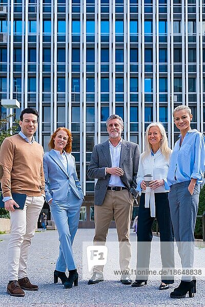 Porträt einer fröhlichen Gruppe von Mitarbeitern  die im Freien in einem Bürogebäude spazieren gehen  mit einem Bürogebäude im Hintergrund